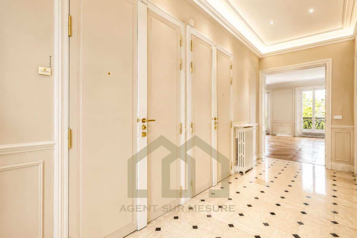 Entrée d'un appartement spacieux avec des portes blanches et un sol en marbre.