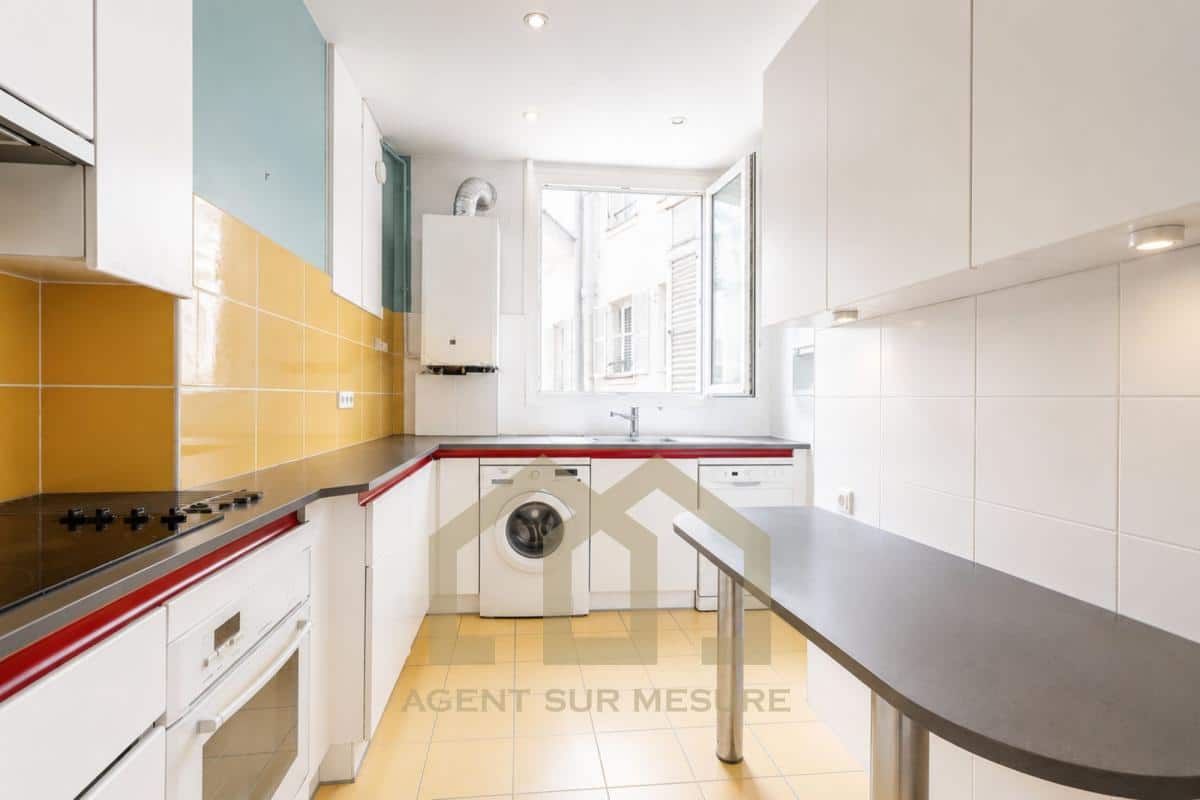 Cuisine moderne avec des éléments en blanc et jaune, fenêtres ouvertes sur l'extérieur.