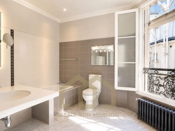 Salle de bain moderne avec baignoire, lavabo et toilettes, fenêtres ouvertes sur un balcon à Paris.