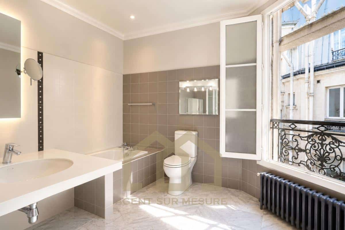 Salle de bain moderne avec baignoire, lavabo et toilettes, fenêtres ouvertes sur un balcon à Paris.