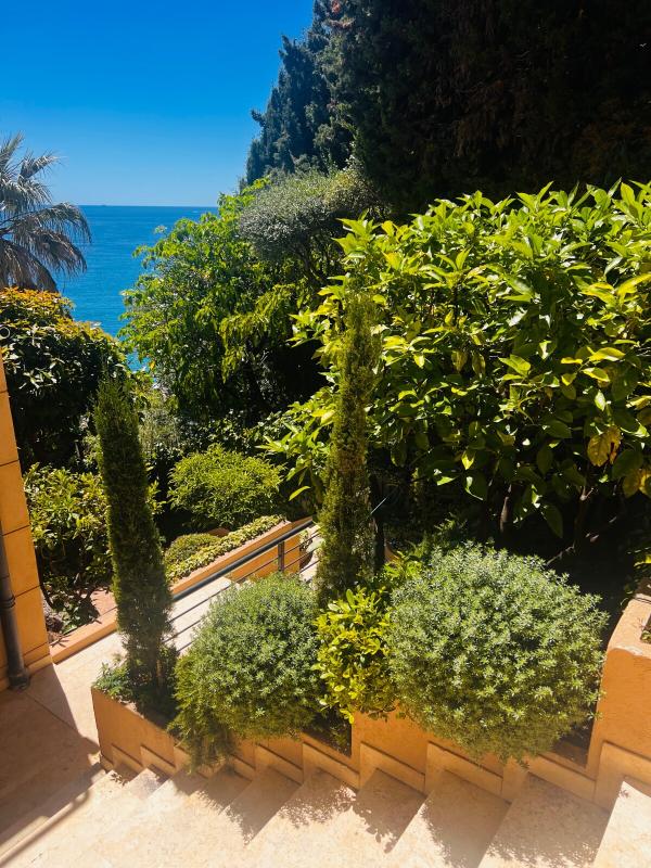 Escaliers menant à un jardin verdoyant avec vue sur la mer Méditerranée.