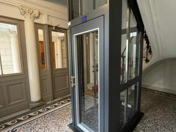 Ascenseur vitré dans un hall d'immeuble bourgeois à Paris, avec des murs en pierre et un sol en mosaïque.