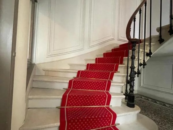Escalier d'un immeuble bourgeois avec moquette rouge et rampe en fer forgé.