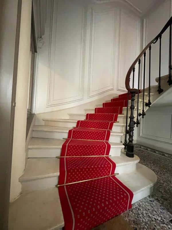Escalier d'un immeuble bourgeois avec moquette rouge et rampe en fer forgé.