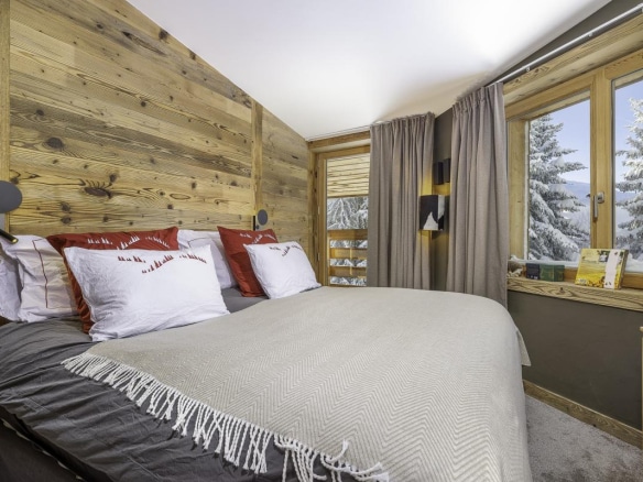 Chambre confortable avec lit double et décoration en bois, fenêtres donnant sur un paysage enneigé.