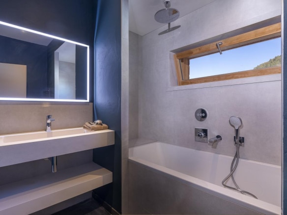 Salle de bain moderne avec baignoire et douche, miroir lumineux, et fenêtre.