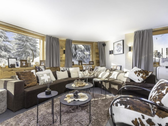 Intérieur d'un chalet confortable avec un salon, des fenêtres donnant sur la neige et des décorations en bois.