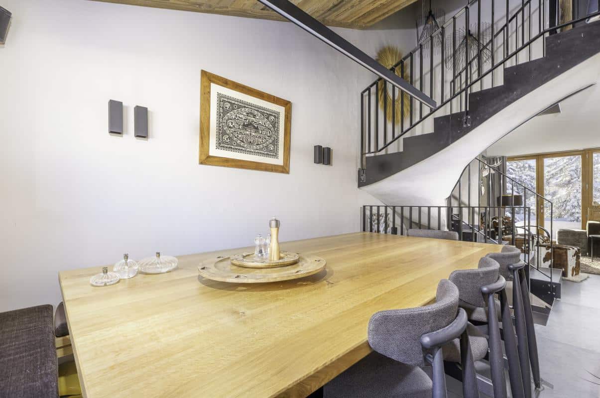 Intérieur du Chalet de la Combe à Avoriaz avec une grande table en bois et un escalier moderne.