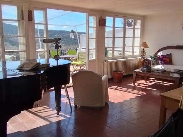 Intérieur d'une vaste demeure avec un piano, un salon lumineux et une vue sur les collines.