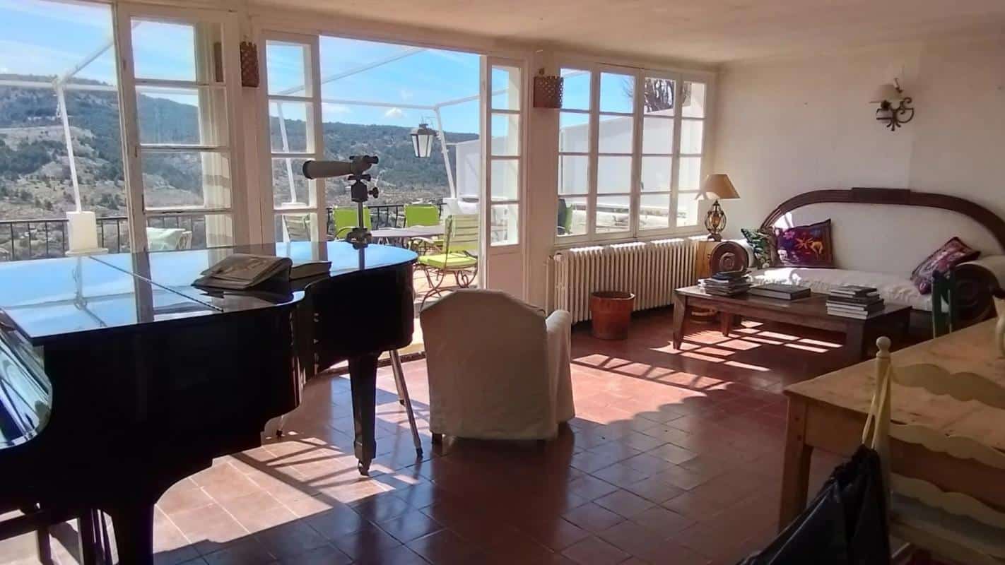 Intérieur d'une vaste demeure avec un piano, un salon lumineux et une vue sur les collines.