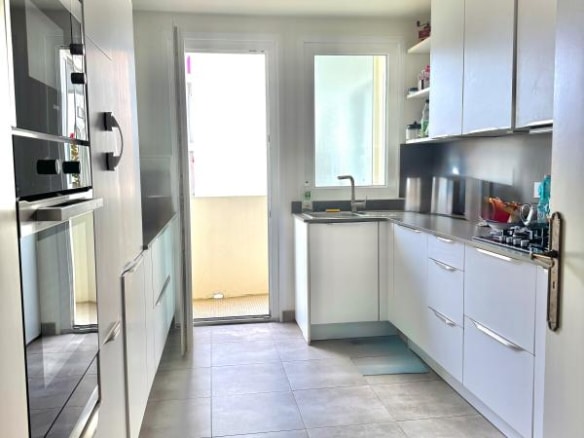 Modern kitchen in a Biarritz apartment with white furniture and windows opening onto a balcony.