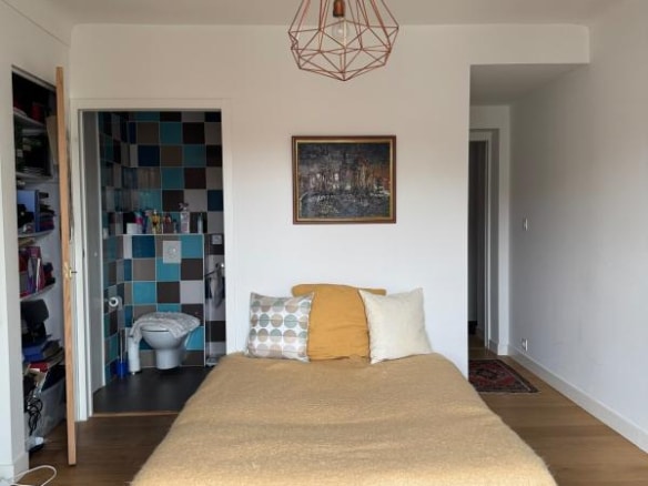 Bedroom in a Biarritz apartment with a bed, a decorated wall and a bathroom visible in the background.