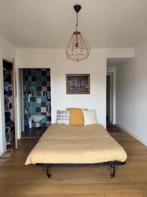 Bedroom in a Biarritz apartment with a bed, a decorated wall and a bathroom visible in the background.