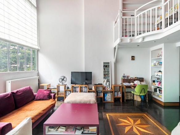 Interior of a bright artist's studio with a high ceiling, living room and workspace.