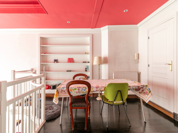 Interior of an artist's studio with a table and chairs, light walls and a red ceiling.