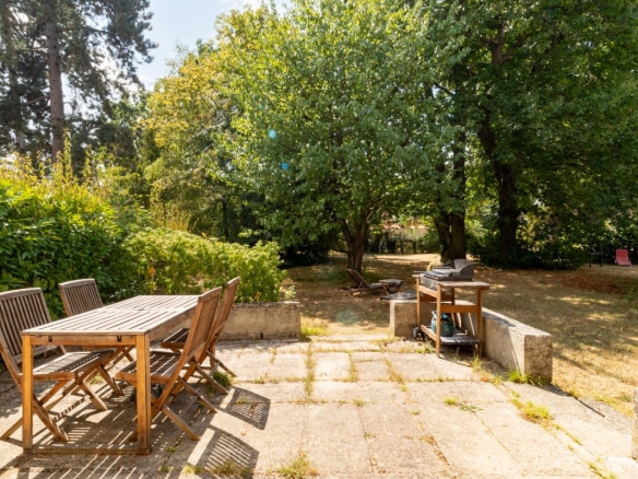 Stone terrace with wooden table and chairs, surrounded by greenery in a private estate.