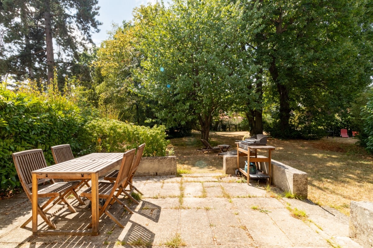Terrace of a house in La Celle-Saint-Cloud Stone terrace with wooden table and chairs, surrounded by greenery in a private estate.