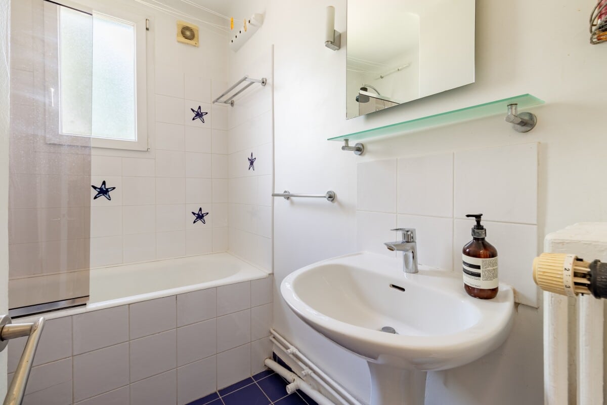 Bathroom in a house in La Celle-Saint-Cloud Bathroom with bathtub, sink and mirror, decorated with white and blue tiles.