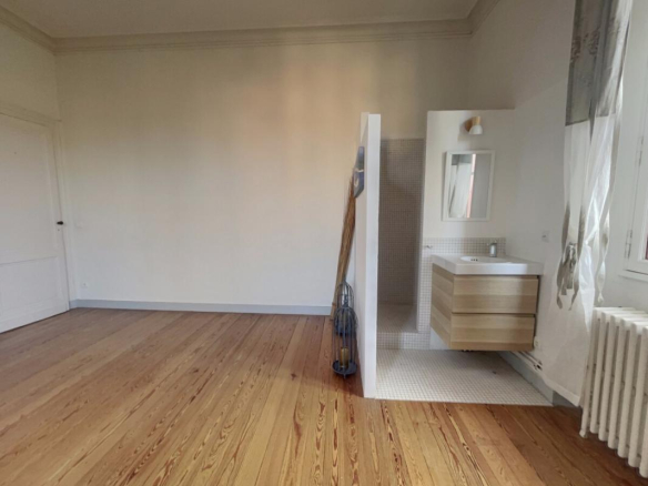 Interior of a renovated apartment with parquet flooring, sink and partially visible shower.