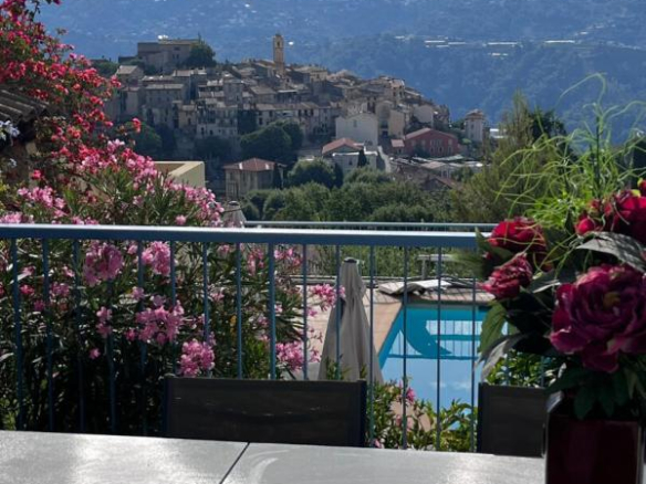 Panoramic view of the village of Gattières from a terrace with swimming pool and flowers in the foreground.
