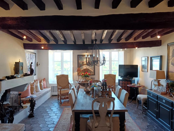 Intérieur d'une maison avec salle à manger, cheminée et fenêtres lumineuses.