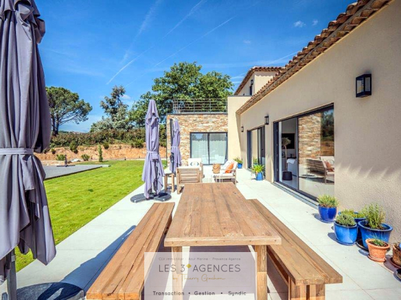 Terrace of a contemporary villa in Grimaud with wooden table and parasols, garden view.