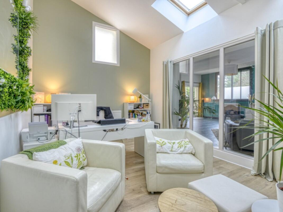 Interior of a spacious apartment with white armchairs, a desk and windows letting in light.