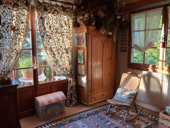 Interior of a traditional chalet with armchair, wooden wardrobe and windows letting in light.