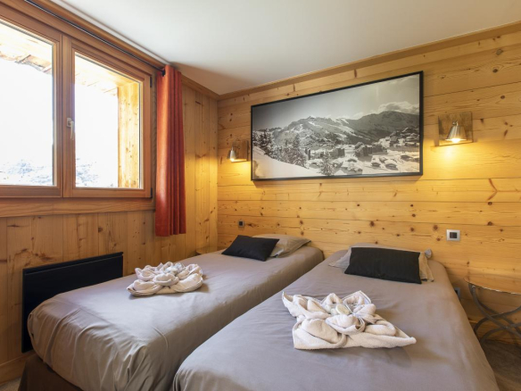 Chambre avec deux lits simples et murs en bois, fenêtre laissant entrer la lumière.