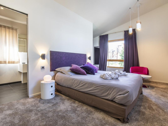 Chambre d'un chalet moderne avec lit, fauteuil et salle de bain attenante.