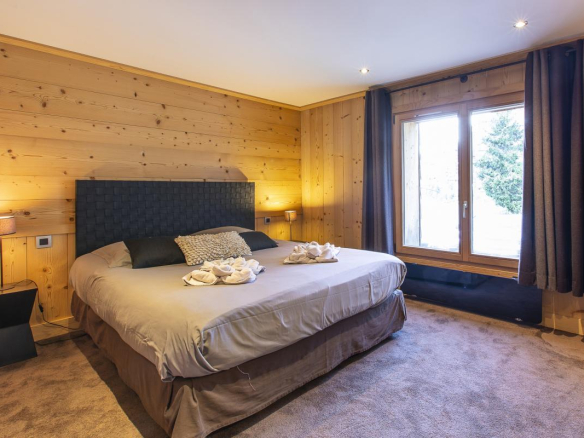 Chambre d'un chalet avec un grand lit et fenêtre donnant sur l'extérieur.
