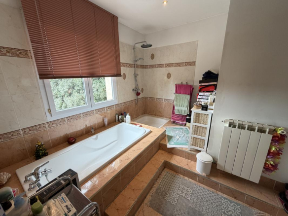 Salle de bain spacieuse avec baignoire et douche, décorée en carrelage beige.