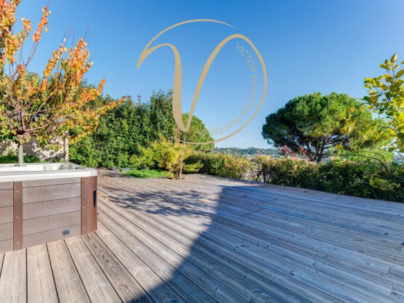 Wooden terrace with jacuzzi, views of hills and sea, surrounded by vegetation.
