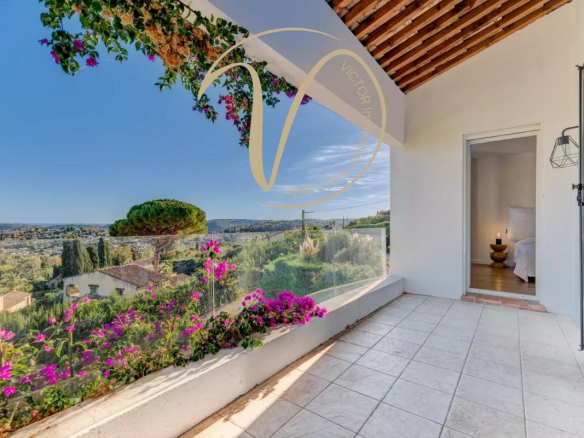 View from a terrace with flowers and a landscape of hills and sea in the background.