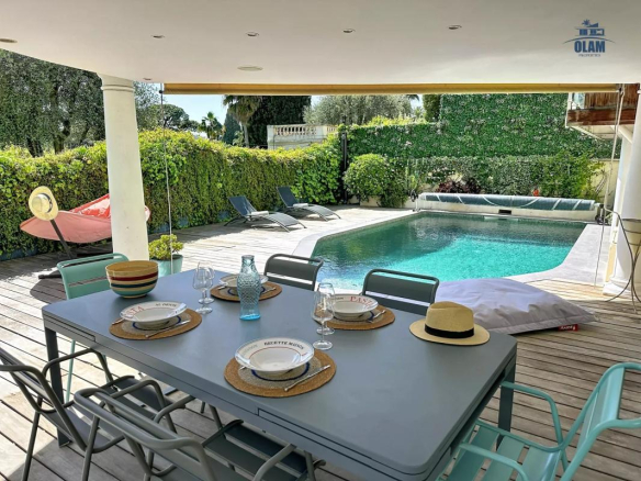Terrasse avec table à manger, chaises et piscine, entourée de verdure à Cannes.