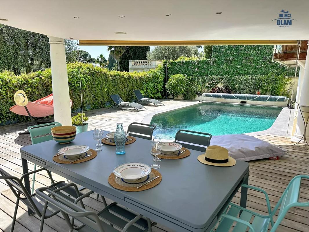Terrasse avec table à manger, chaises et piscine, entourée de verdure à Cannes.