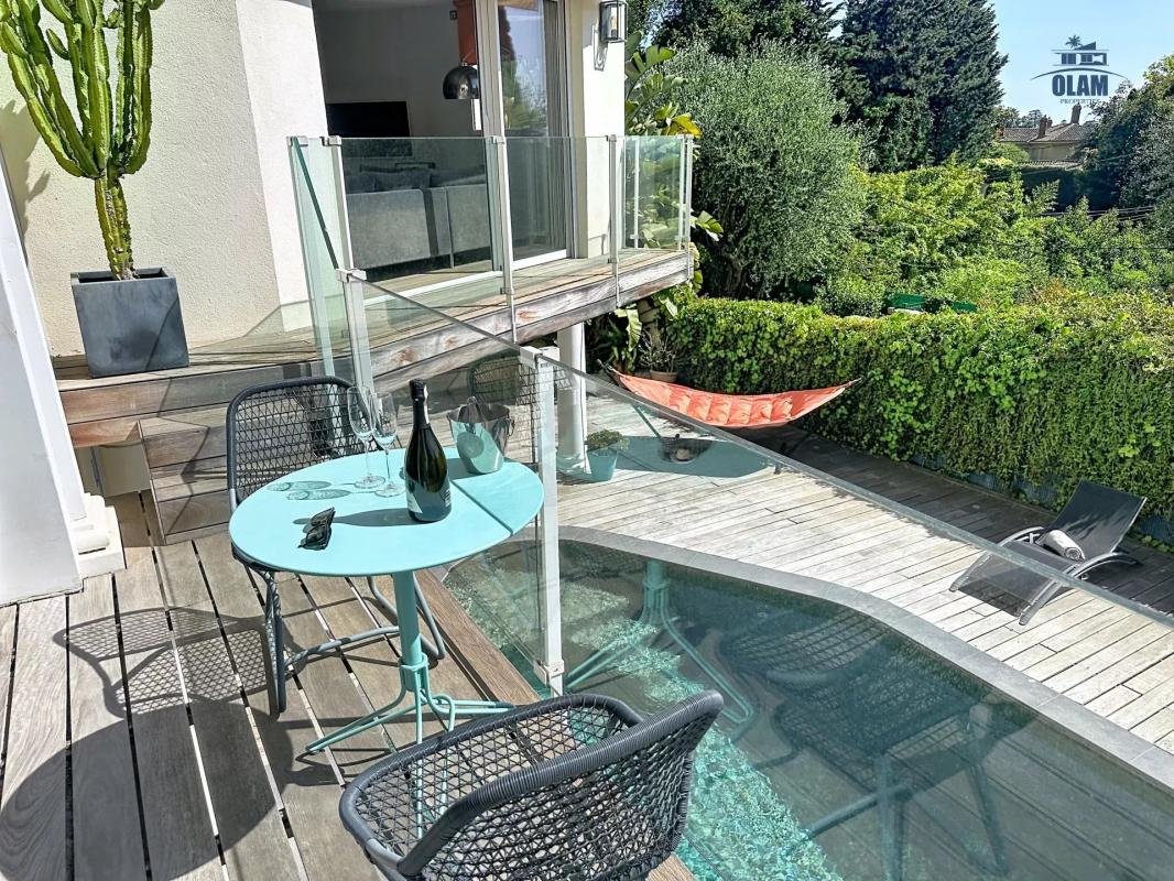 Terrasse avec piscine et mobilier extérieur dans une villa à Cannes, entourée de verdure.