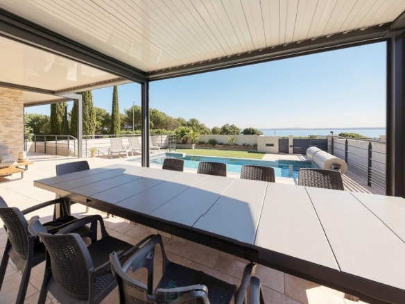 Terrasse d'une villa contemporaine avec piscine, chaises et vue dégagée sur la nature.