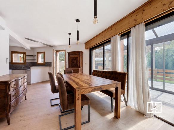 Intérieur d'une maison rénovée avec une grande table en bois et des fenêtres donnant sur le jardin.