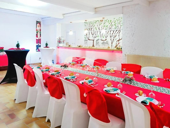 Salle à manger décorée pour un événement avec des tables couvertes de rouge et des chaises blanches.