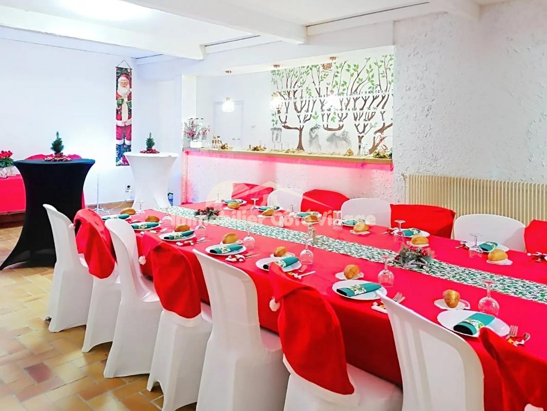Salle à manger décorée pour un événement avec des tables couvertes de rouge et des chaises blanches.