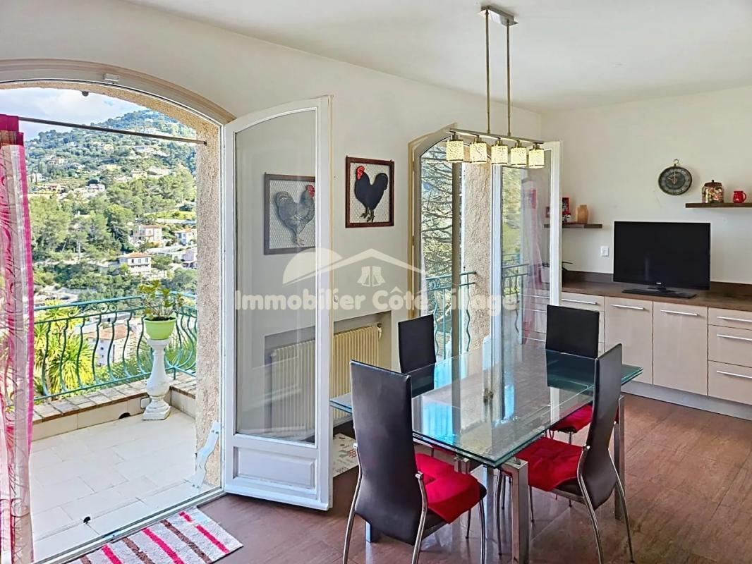 Salle à manger lumineuse avec vue sur les collines, fenêtres ouvertes, mobilier moderne.