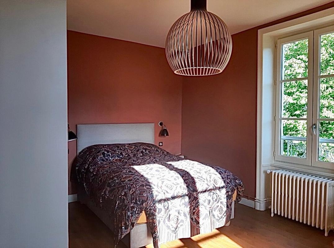 Chambre d'une maison rénovée à Beaujeu avec lit et fenêtre donnant sur un jardin arboré.