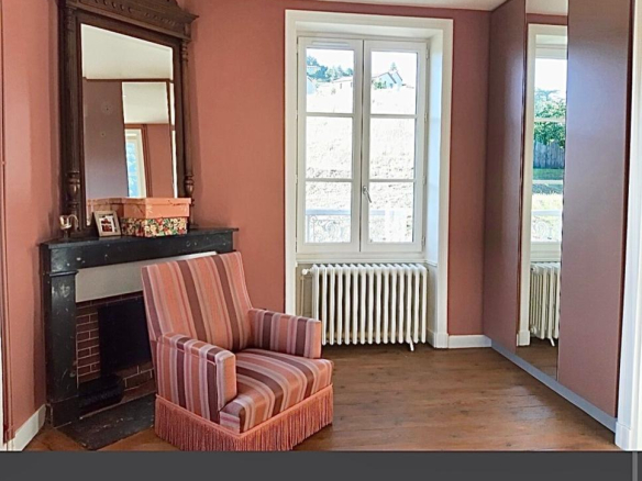 Intérieur d'une maison rénovée à Beaujeu, avec un fauteuil rayé et une cheminée en pierre.