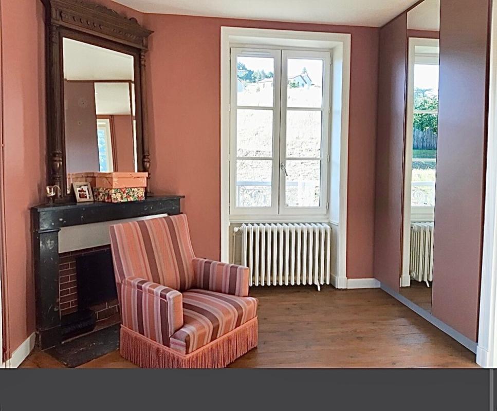 Intérieur d'une maison rénovée à Beaujeu, avec un fauteuil rayé et une cheminée en pierre.
