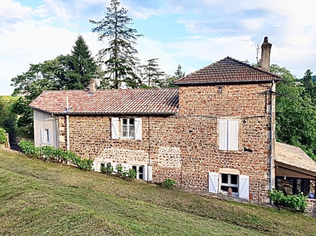 Maison en pierre rénovée à Beaujeu, entourée de verdure, avec un terrain arboré.