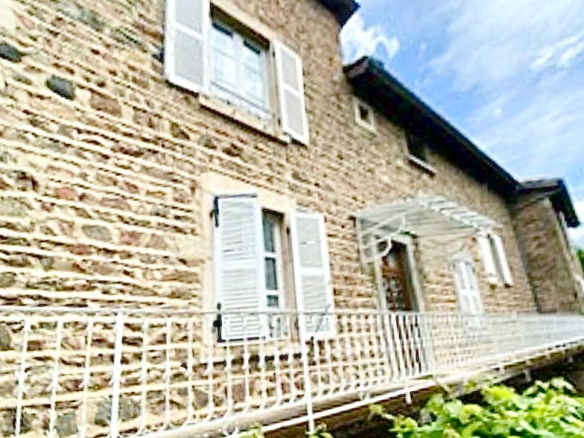 Façade en pierre d'une maison rénovée à Beaujeu, avec balustrade et fenêtres blanches.