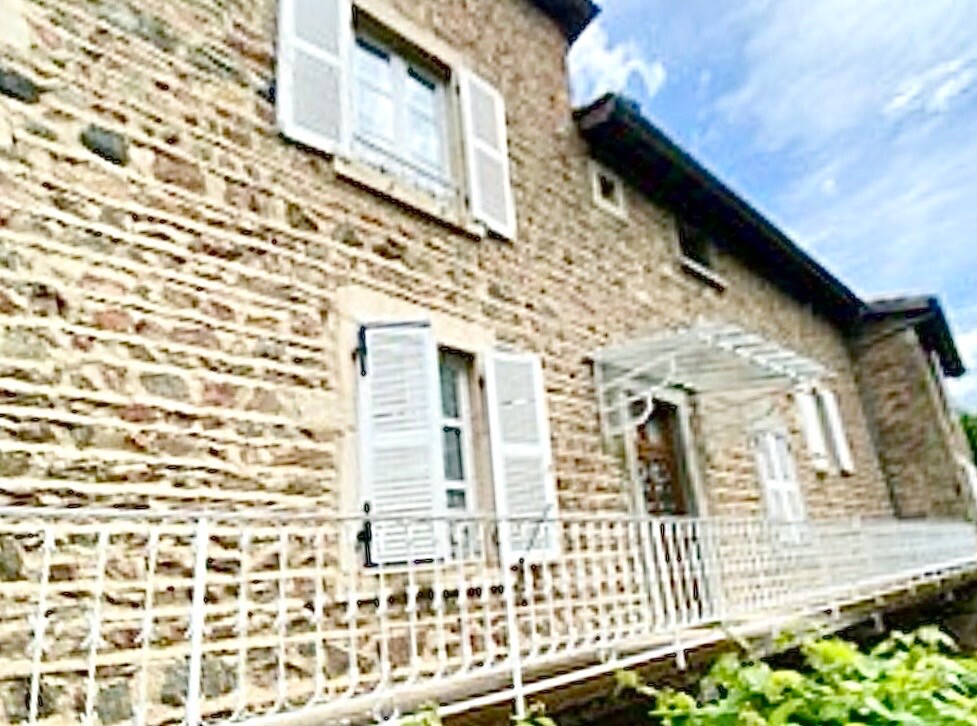 Façade en pierre d'une maison rénovée à Beaujeu, avec balustrade et fenêtres blanches.