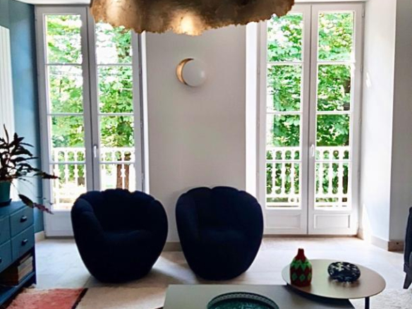 Intérieur d'une maison rénovée à Beaujeu, avec des fauteuils et de grandes fenêtres donnant sur un jardin.