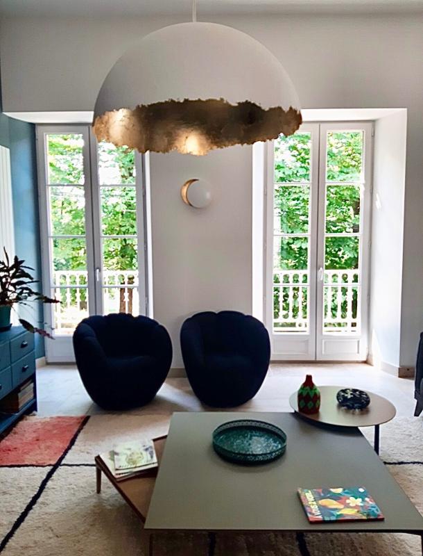 Intérieur d'une maison rénovée à Beaujeu, avec des fauteuils et de grandes fenêtres donnant sur un jardin.